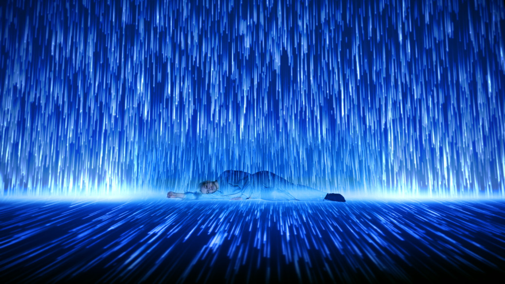 A woman lying on the floor of a studio while visual blue light is raining down on her