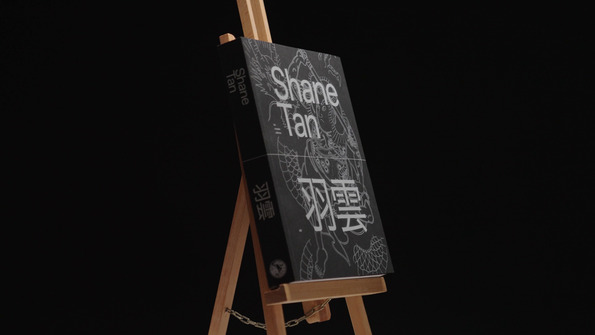 A book by shane tan on a bookstand in front of a black background.